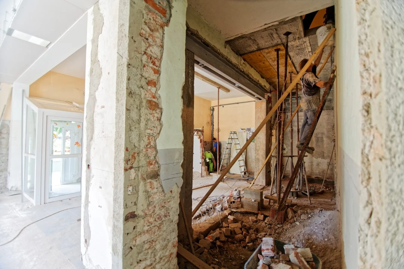 A room with a ladder and a wall of bricks where a roofer works by standing on a ladder
