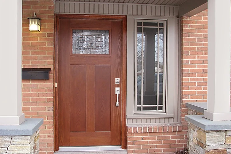 A wooden front door with a decorative glass panel near the top complements the brick wall, underlining the quality craftsmanship typical in New Castle County, DE. Beside it, a vertical window with geometric designs adds charm while a small light fixture and mail slot complete the inviting entrance.